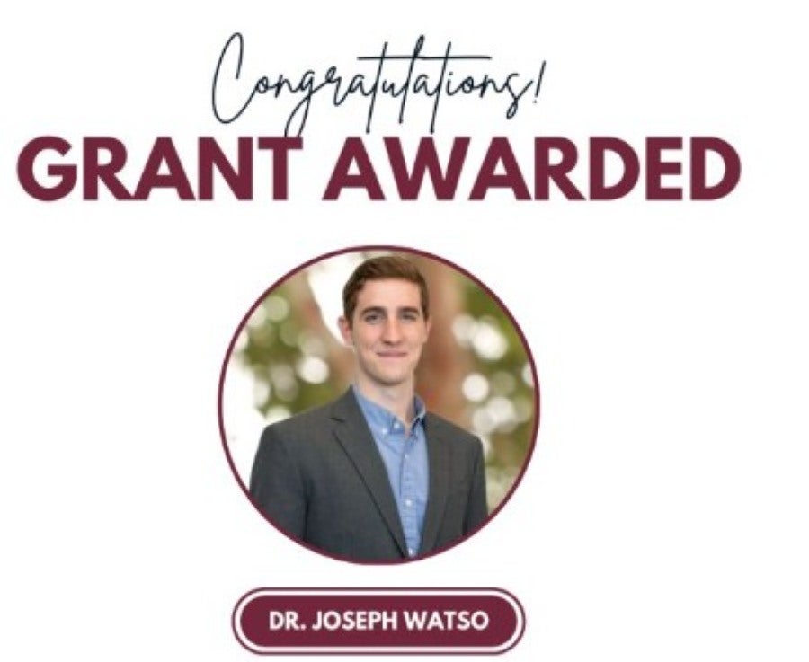 Graphic featuring a headshot of Dr. Joseph Watso set inside a circular maroon frame against a white background. Black cursive script at the top reads "Congratulations!" above large, maroon capital letters that state "GRANT AWARDED." At the bottom, "DR. JOSEPH WATSO" is displayed in white text inside a rounded maroon pill banner. Dr. Watso, a young man with brown hair wearing a blue button-down shirt and a dark grey suit jacket, is smiling toward the camera.