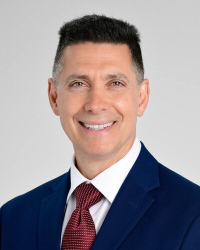 Headshot of Tom Rifai smiling while wearing a navy suit and red tie.
